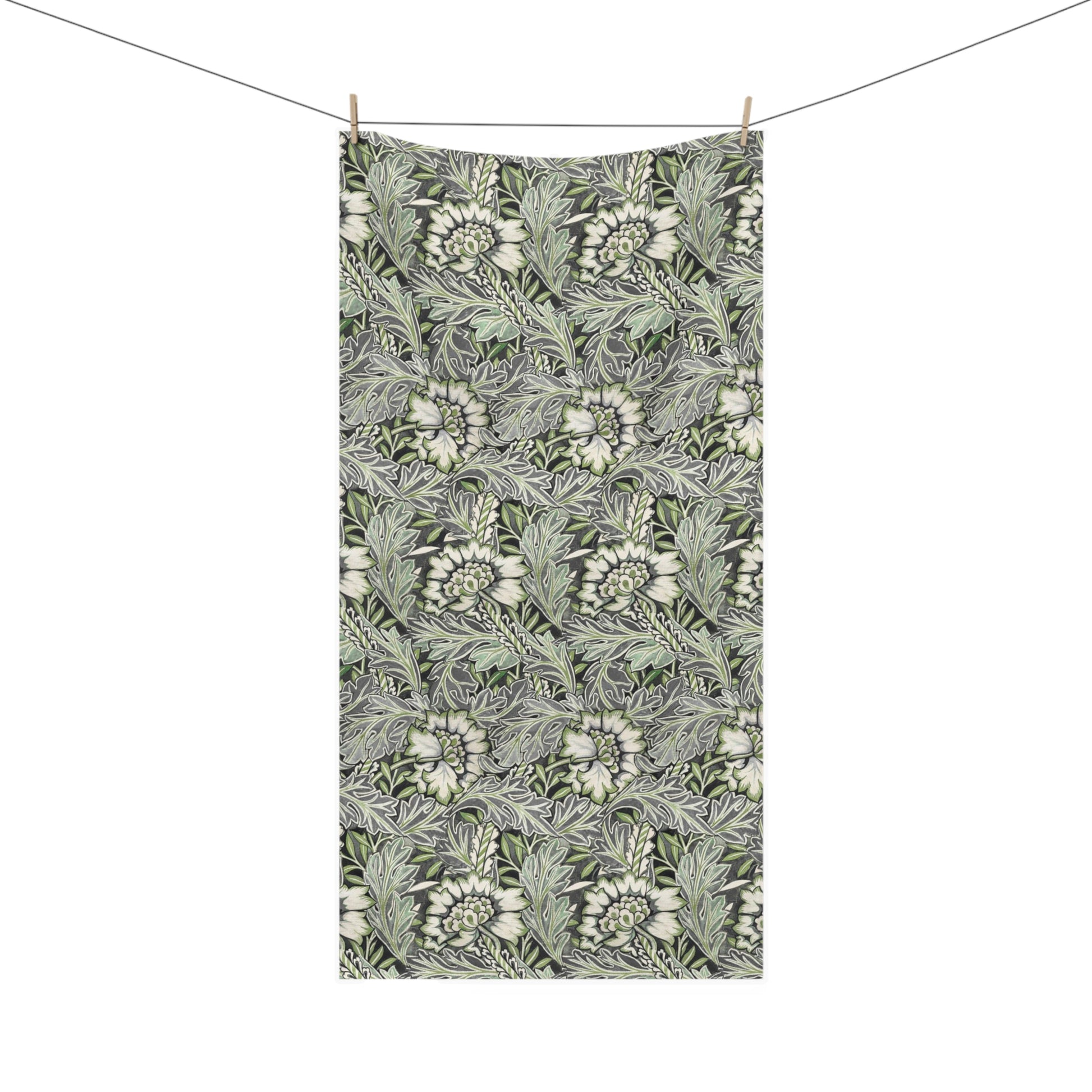 A rectangular fabric towel with a dense botanical pattern of white flowers and green leaves on a dark gray background, hanging from two wooden clothespins on a thin wire against a plain white background.
