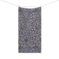 A rectangular bath towel with an all-over floral and botanical pattern in navy blue and warm beige, hanging from two wooden clothespins on a string against a plain white background.