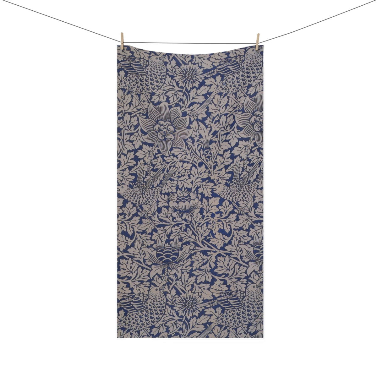 A rectangular bath towel with an all-over floral and botanical pattern in navy blue and warm beige, hanging from two wooden clothespins on a string against a plain white background.