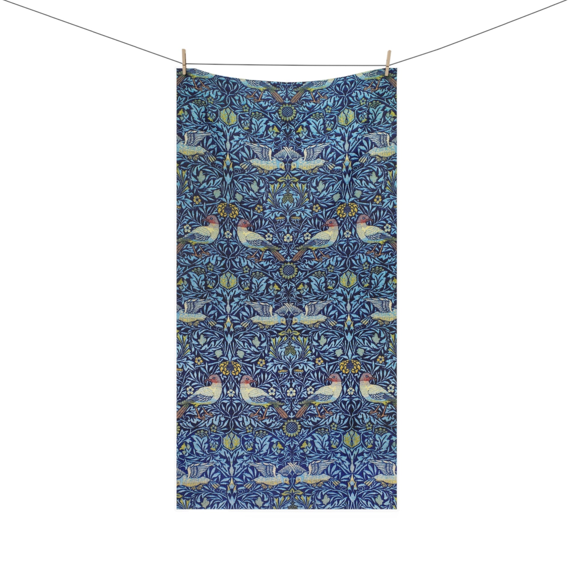 A rectangular towel hanging from a clothesline with two wooden clips, featuring a dense blue floral and bird pattern with pink, white, and yellow details on a white background.