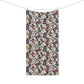 A rectangular bath towel with an all-over floral and botanical pattern hangs from a clothesline with two wooden clips against a plain white background.