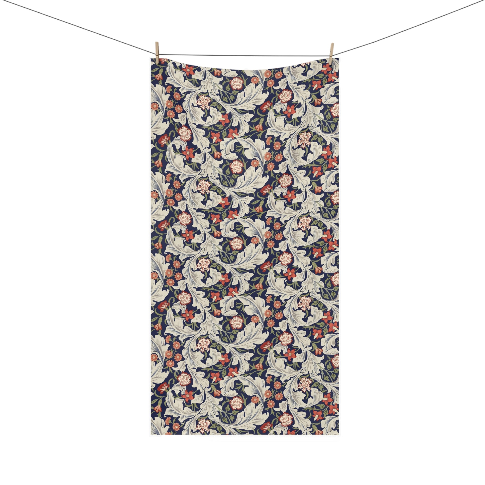 A rectangular bath towel with an all-over floral and botanical pattern hangs from a clothesline with two wooden clips against a plain white background.