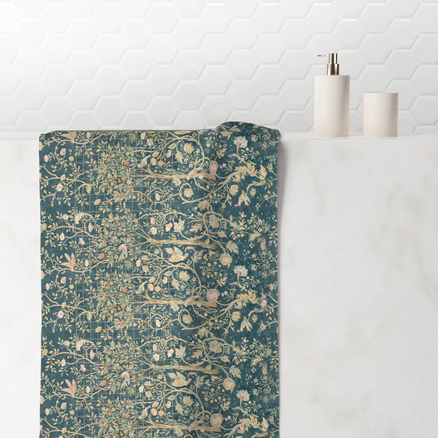 A bath towel with a detailed botanical and bird pattern in teal, beige, and muted pink, draped over a white marble bathroom counter next to a white soap dispenser.