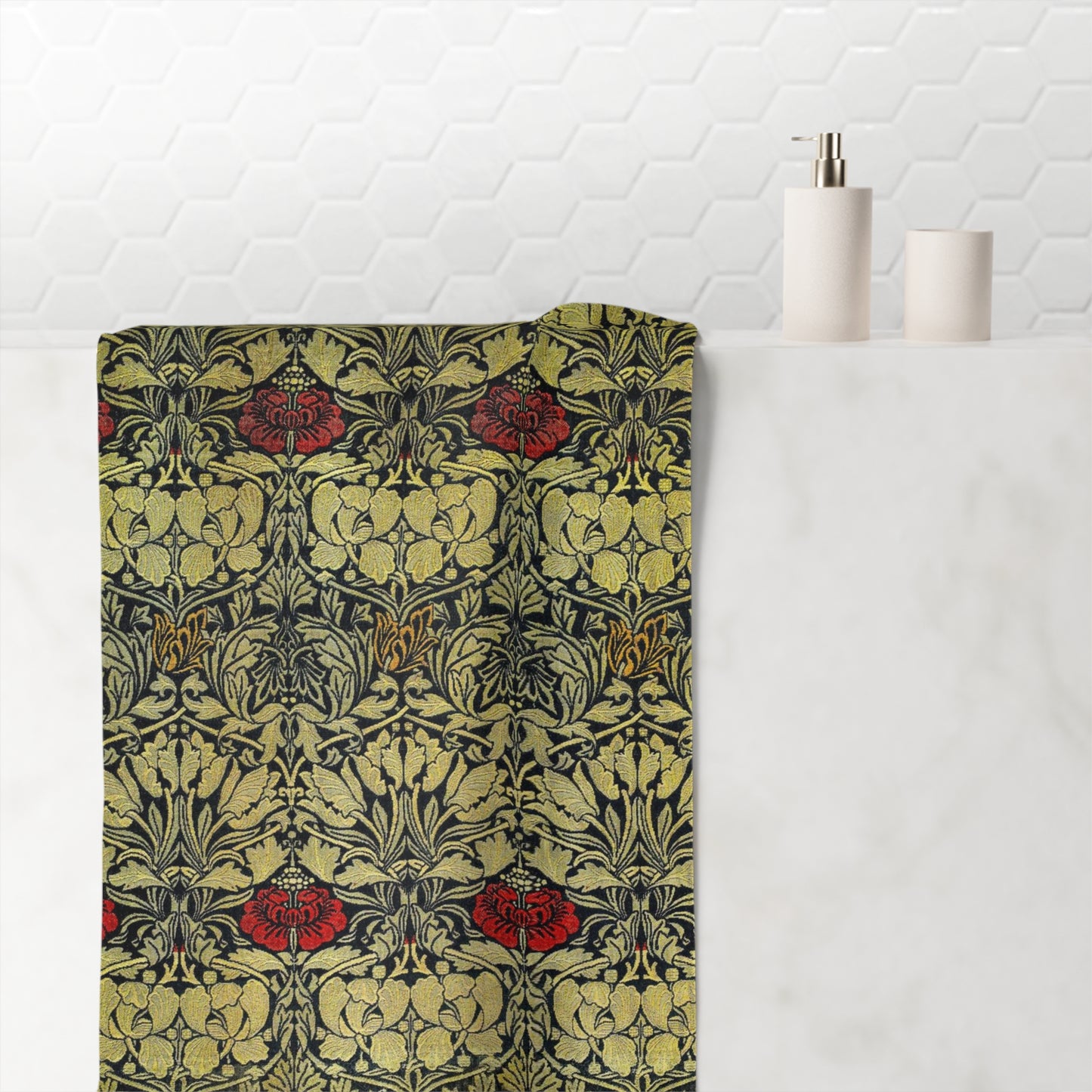 A folded bath towel with an intricate Art Nouveau pattern in olive green, black, and red, draped over a white marble bathroom counter next to a white soap dispenser and cup.