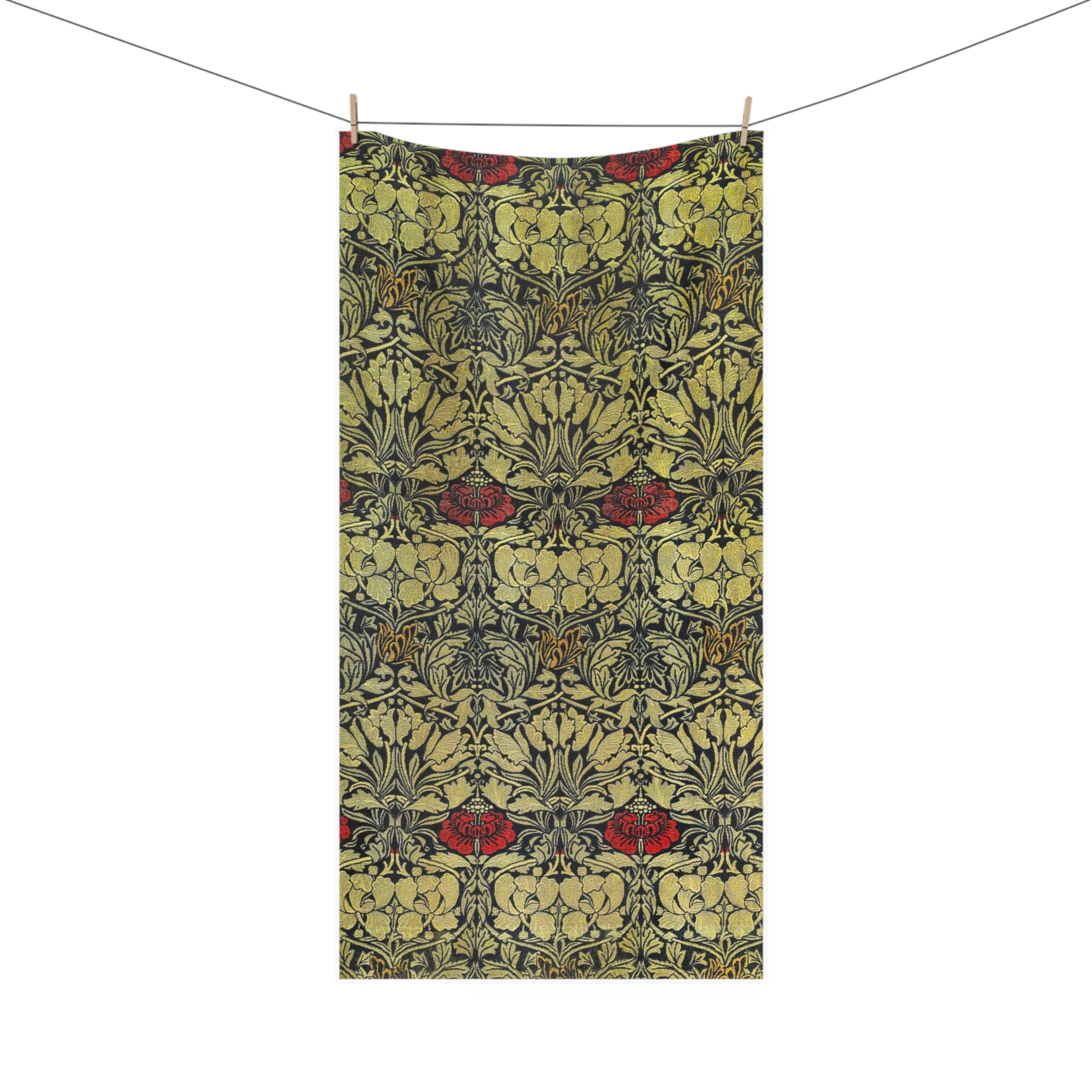A rectangular bath towel from a clothesline with two wooden clips, featuring an ornate repeating floral pattern in muted yellow, olive green, charcoal gray, and red accents, shown against a plain white background.