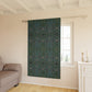 Patterned green curtain hanging in a room with a sofa and window.