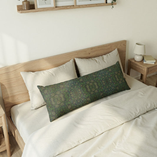 A long rectangular lumbar pillow with an intricate William Morris & Co green and brown paisley pattern rests on a bed with cream bedding and white pillows in a minimalist, warm-toned bedroom.