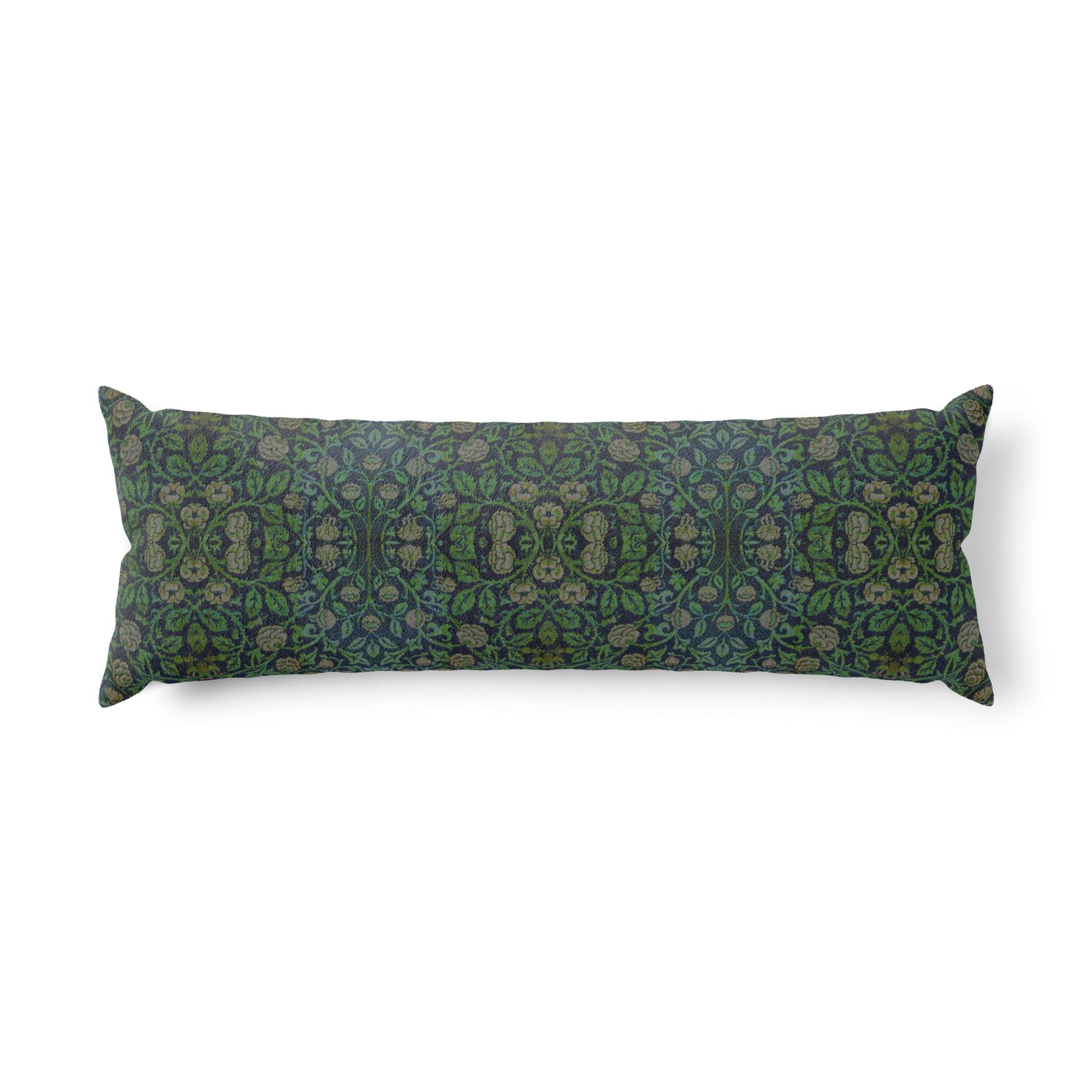 A long rectangular lumbar pillow with an intricate William Morris & Co green and brown paisley pattern rests on a bed with cream bedding and white pillows in a minimalist, warm-toned bedroom.