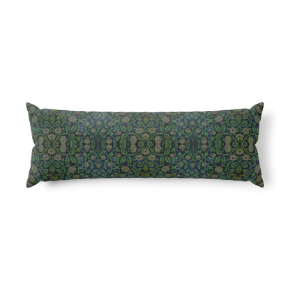 A long rectangular lumbar pillow with an intricate William Morris & Co green and brown paisley pattern rests on a bed with cream bedding and white pillows in a minimalist, warm-toned bedroom.