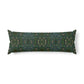 A long rectangular lumbar pillow with an intricate William Morris & Co green and brown paisley pattern rests on a bed with cream bedding and white pillows in a minimalist, warm-toned bedroom.