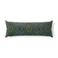A long rectangular lumbar pillow with an intricate William Morris & Co green and brown paisley pattern rests on a bed with cream bedding and white pillows in a minimalist, warm-toned bedroom.