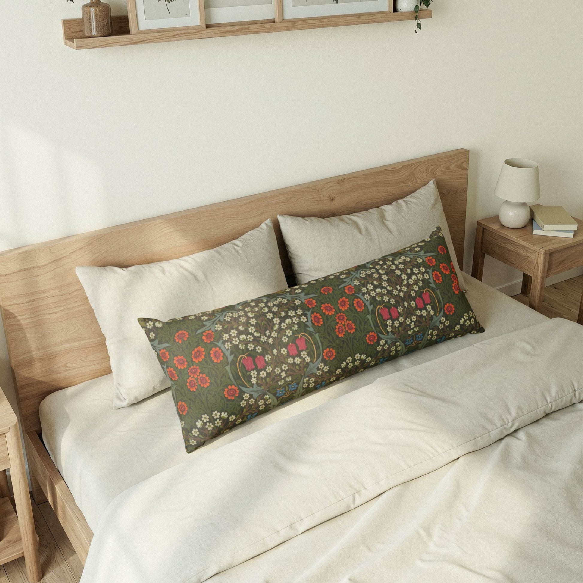 A rectangular lumbar pillow with a green floral pattern rests on a bed with white bedding and two white pillows in a minimalist bedroom setting.
