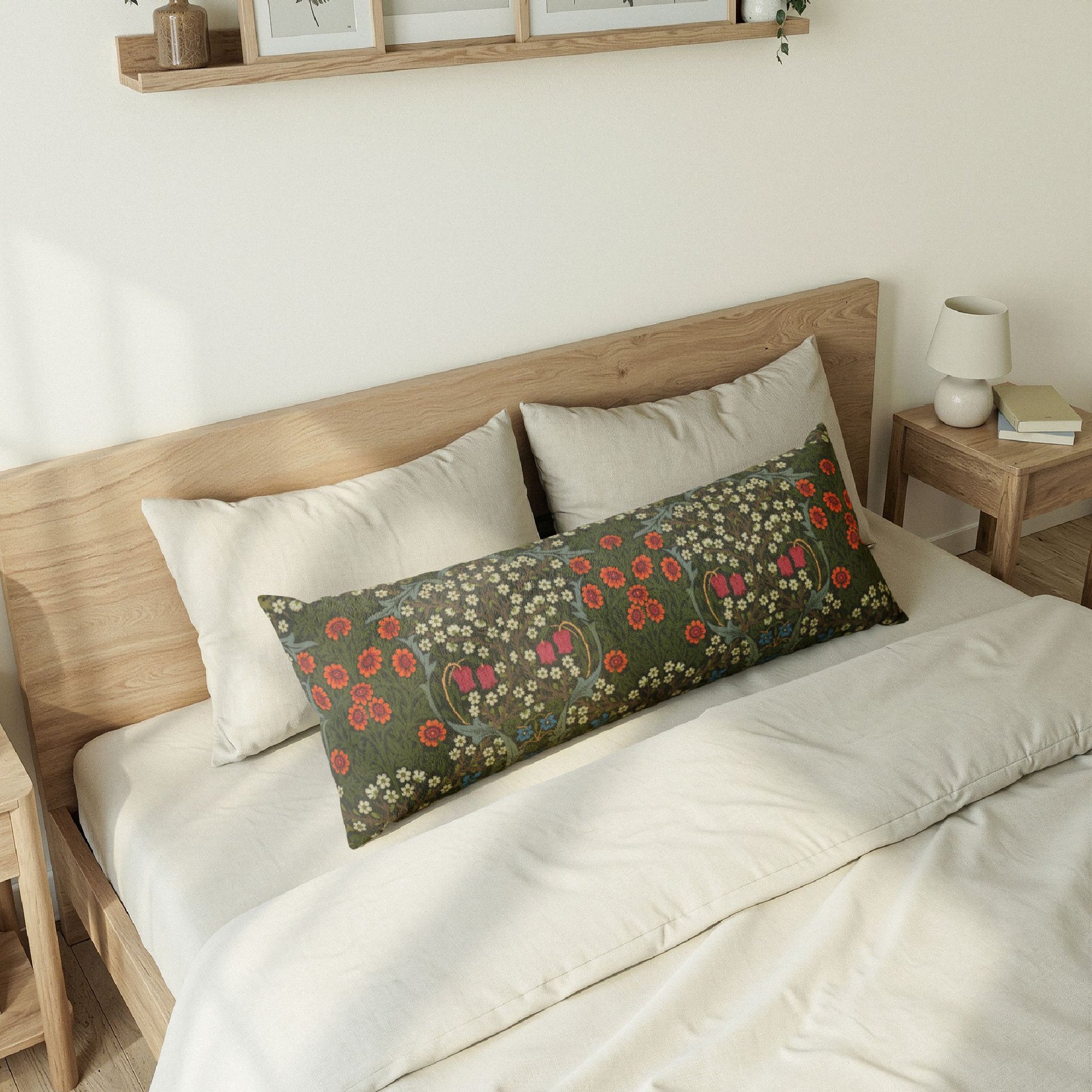A long rectangular lumbar pillow with a dark green floral pattern, styled on a bed with white bedding and a light wood headboard in a bright bedroom setting.