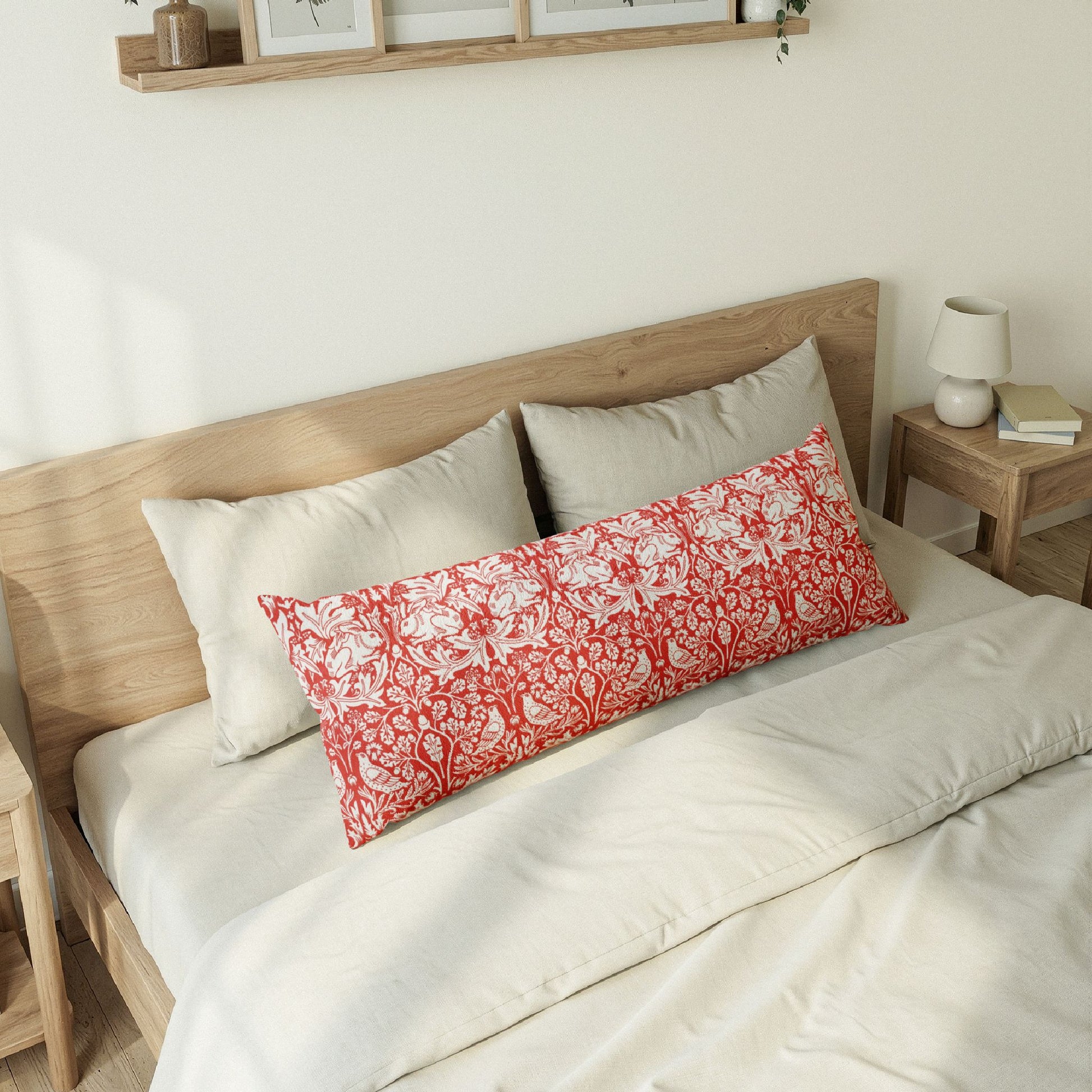 Bed with wooden headboard and decorative pillows, including a red floral pillow in a William Morris pattern called Brer Rabbit.
