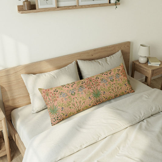A long rectangular lumbar pillow with a pink floral and botanical pattern, styled on a bed with white bedding and a light wood headboard in a warm, minimalist bedroom setting.