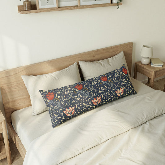A long decorative lumbar pillow with a navy blue background and a detailed floral vine pattern in orange, red, and gold, styled on a bed with cream bedding and wooden headboard.