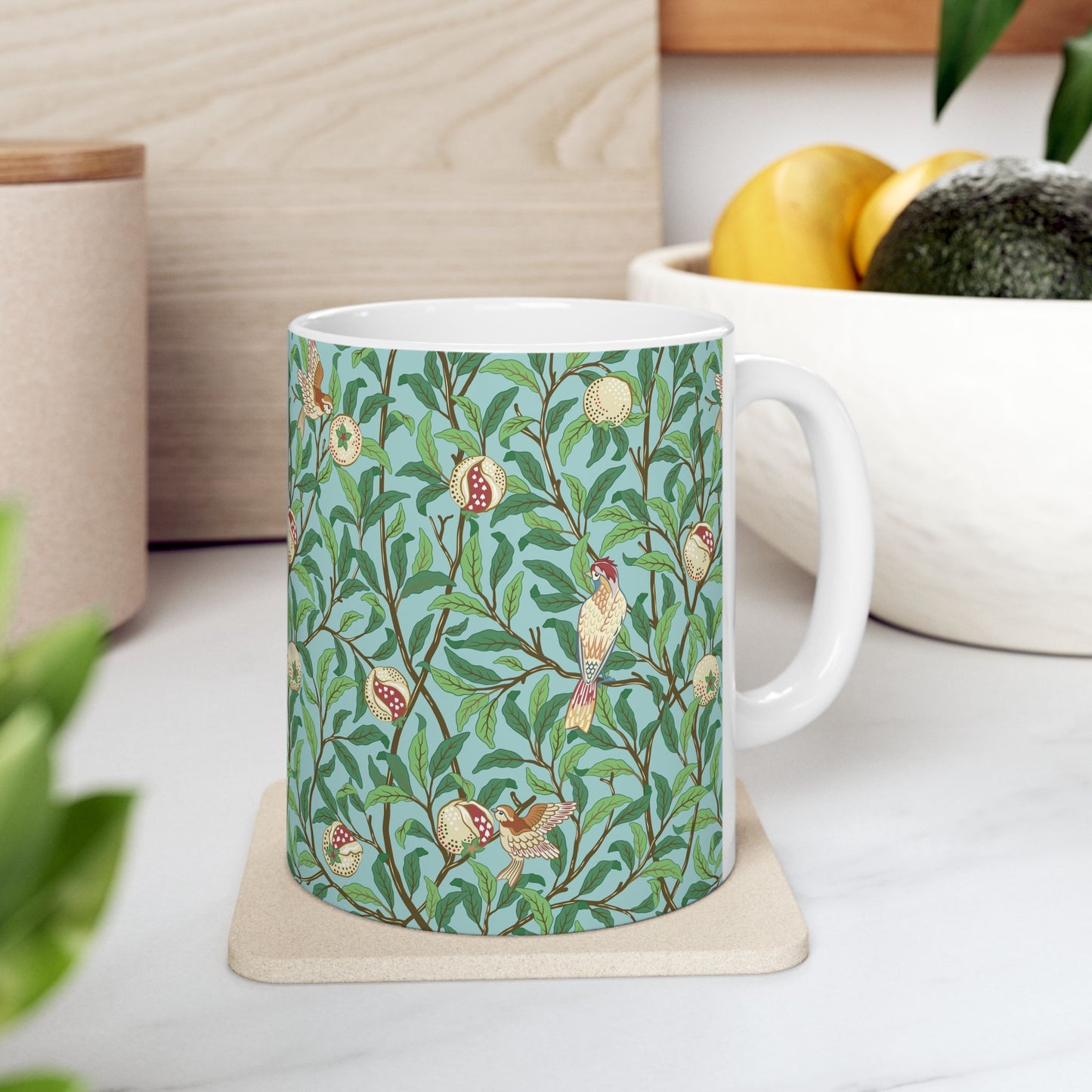 A ceramic mug with a blue background featuring a floral pattern of birds and pomegranates.