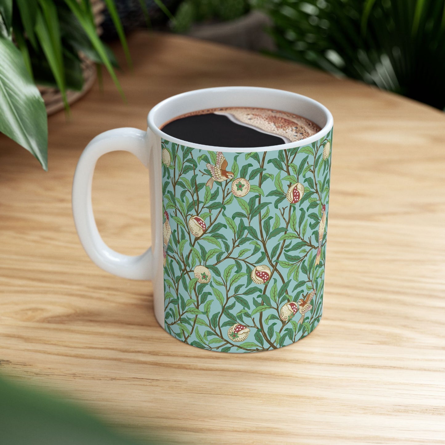 A ceramic mug with a blue background featuring a floral pattern of birds and pomegranates.