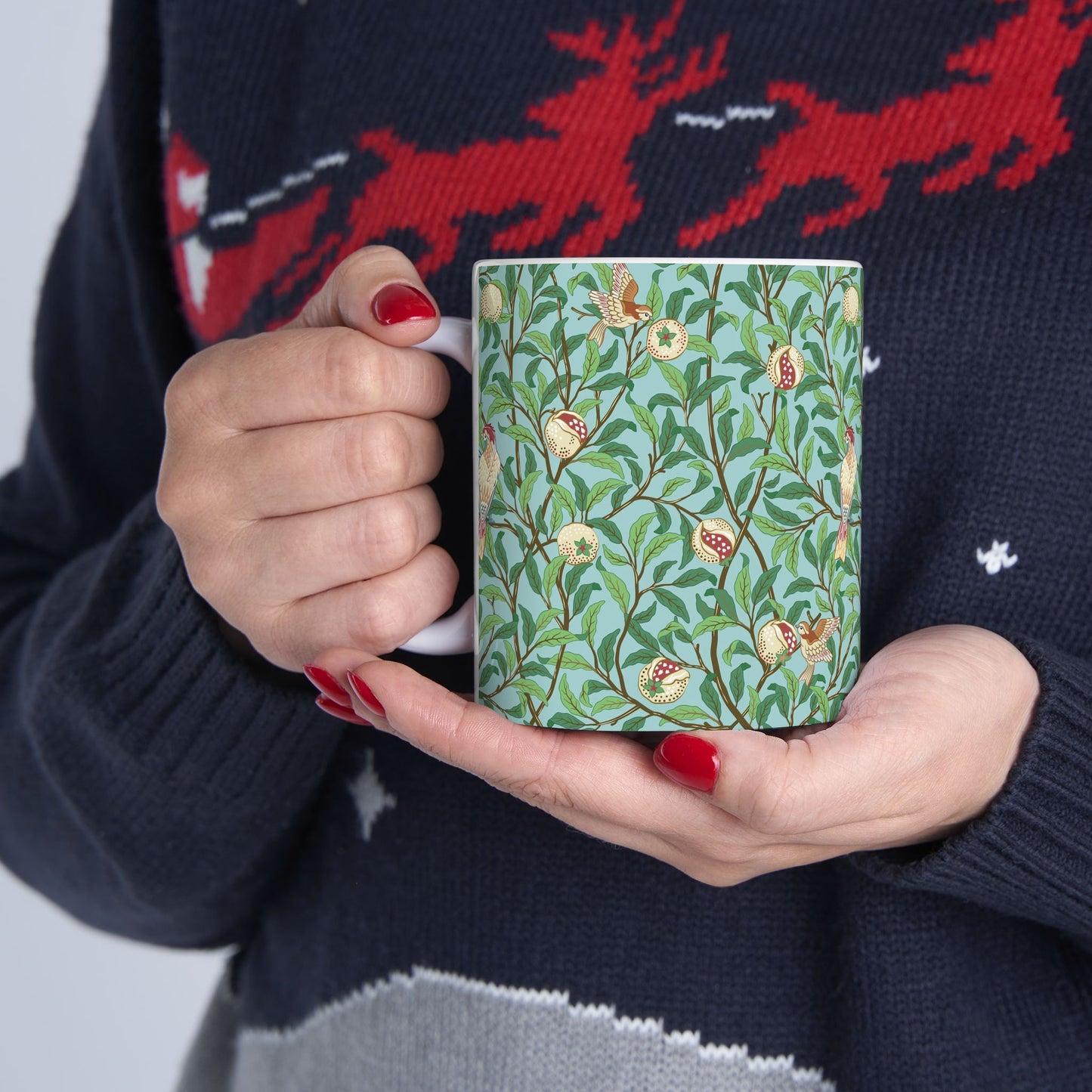 A ceramic mug with a blue background featuring a floral pattern of birds and pomegranates.