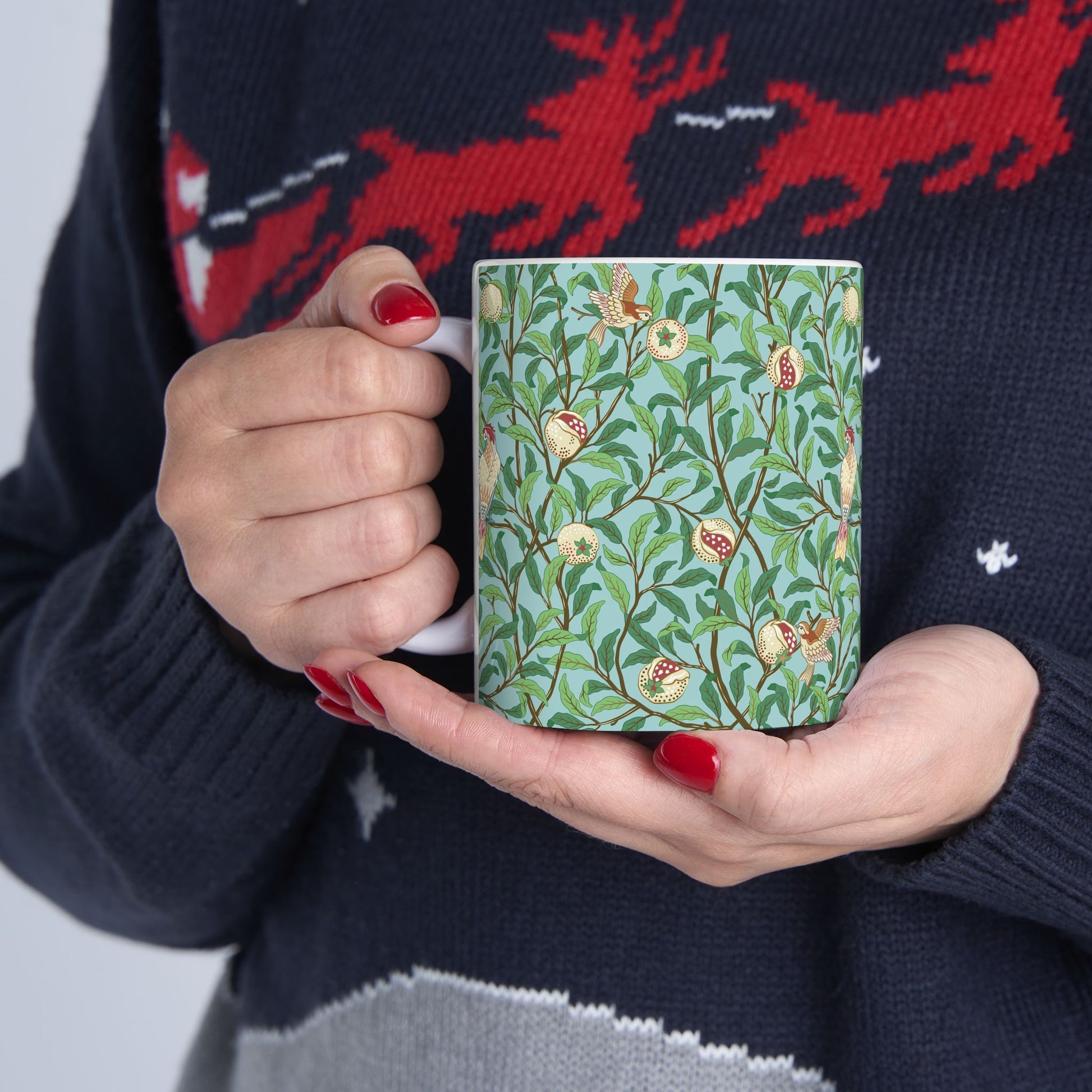 A ceramic mug with a blue background featuring a floral pattern of birds and pomegranates.
