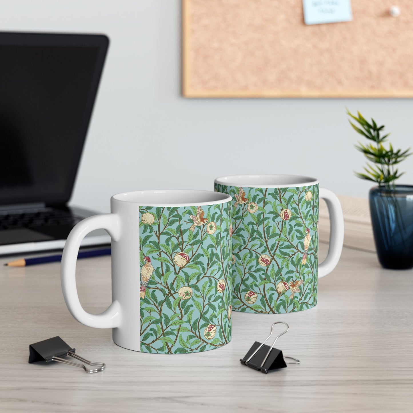 A ceramic mug with a blue background featuring a floral pattern of birds and pomegranates.