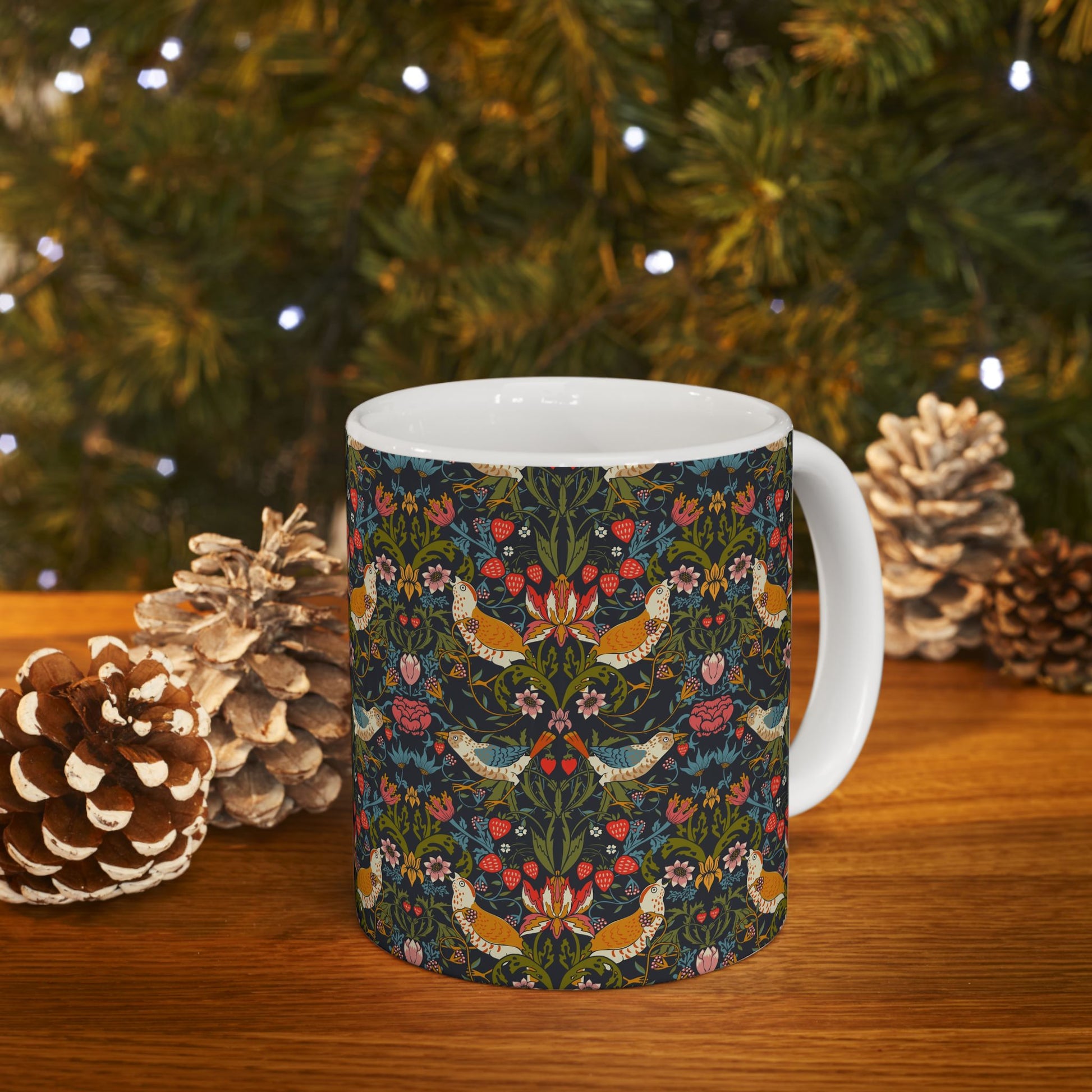 Mug with floral and bird pattern on a wooden surface with pinecones and a Christmas tree in the background.
