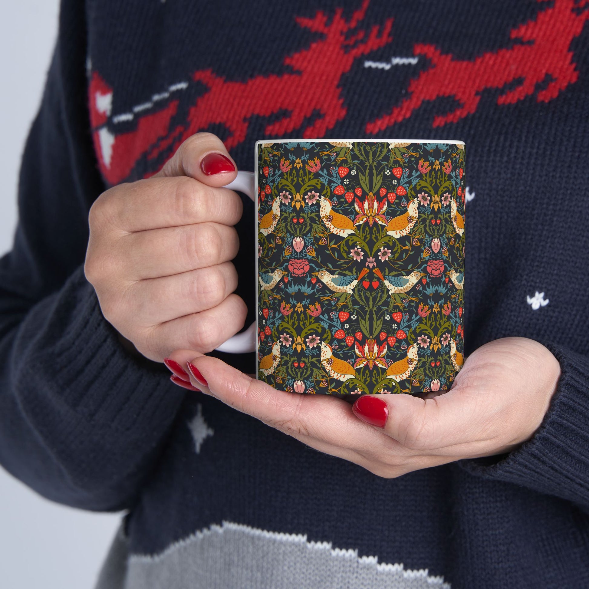 Person holding a patterned mug with a dark sweater featuring red deer design.