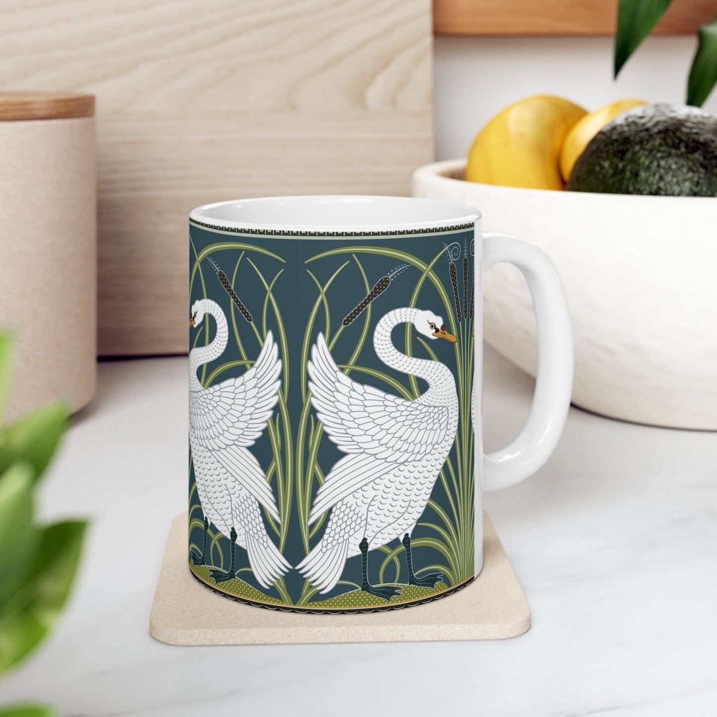 A ceramic mug with a design of two white swans on a green and blue background, inspired by the art of William Morris.