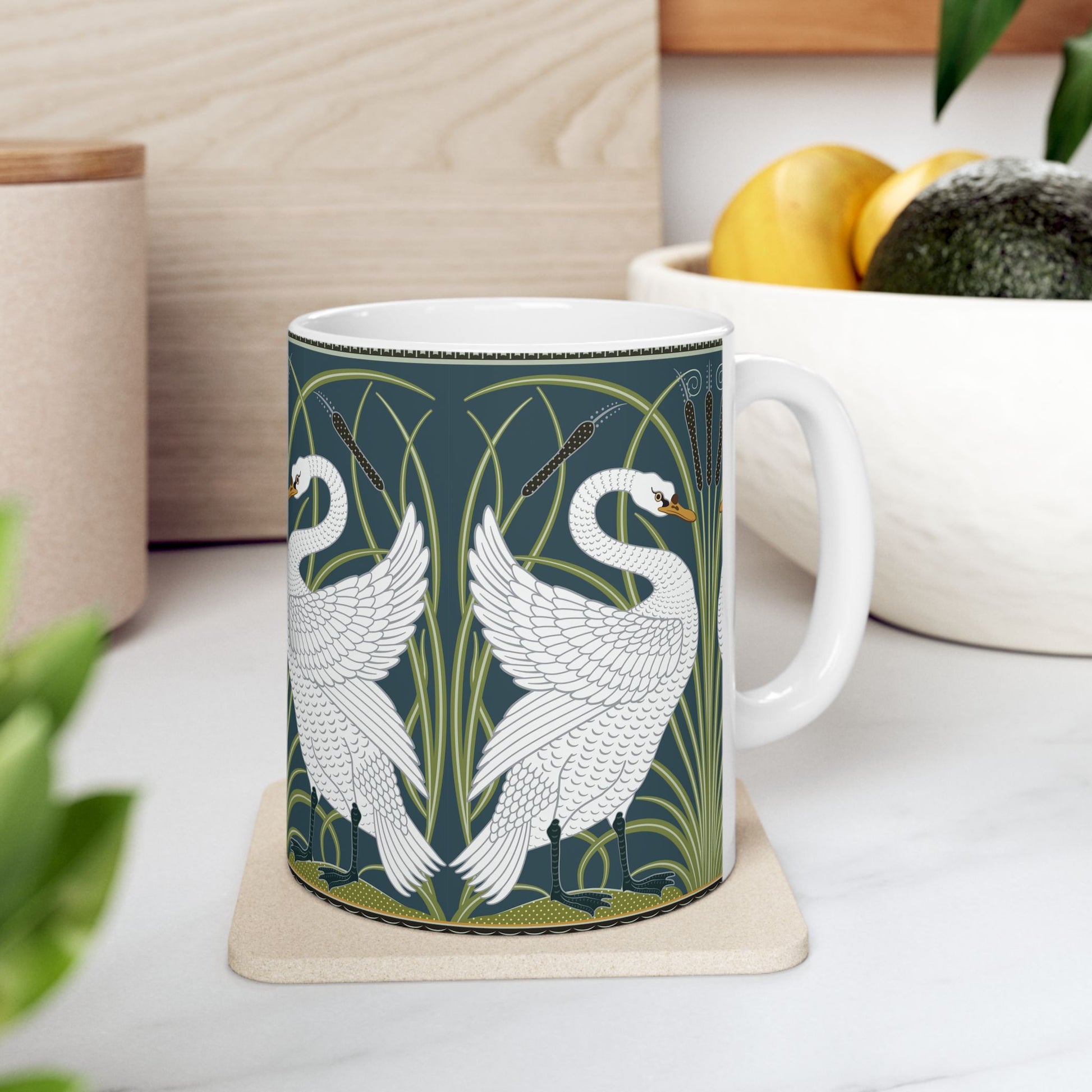 A ceramic mug with a design of two white swans on a green and blue background, inspired by the art of William Morris.