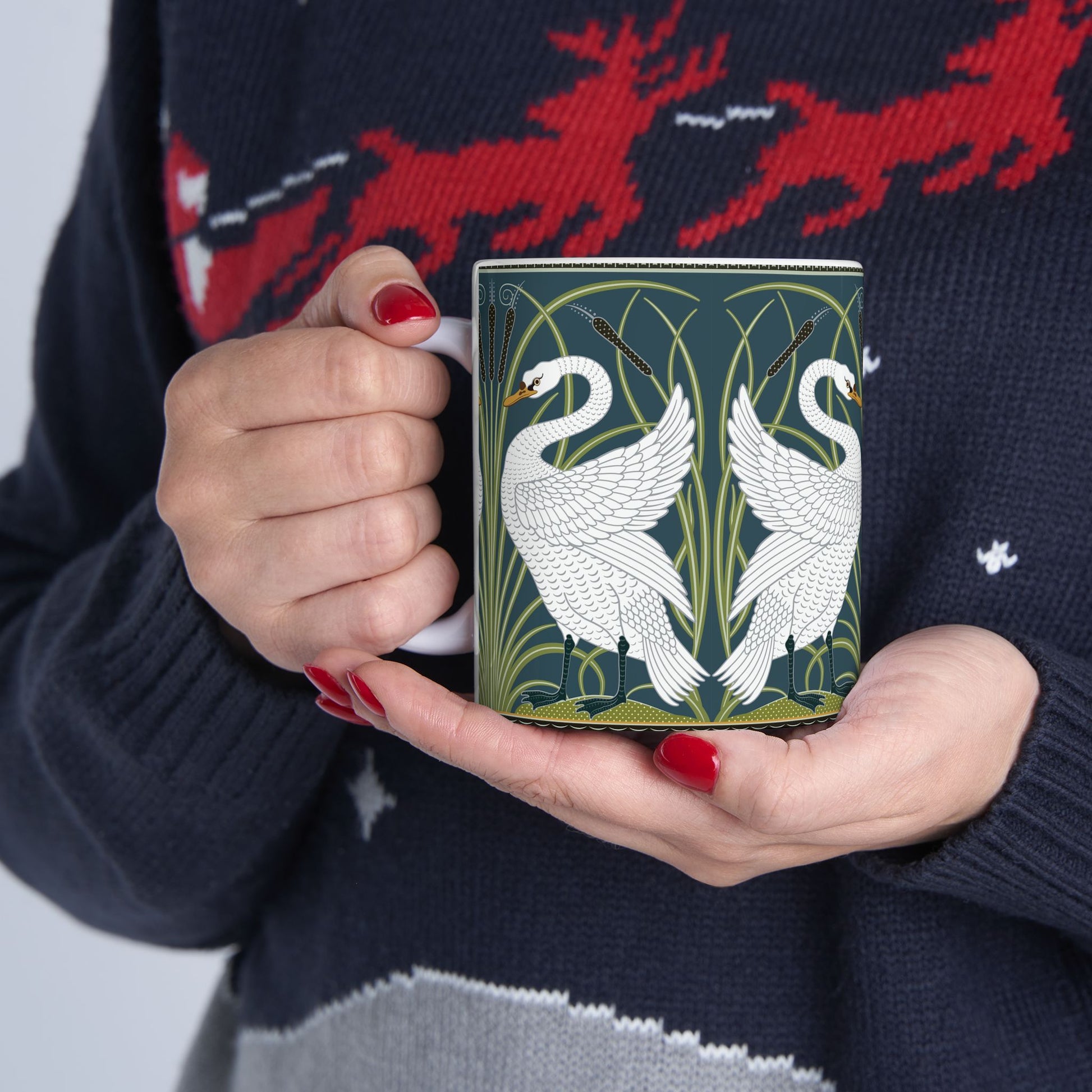 A ceramic mug with a design of two white swans on a green and blue background, inspired by the art of William Morris.