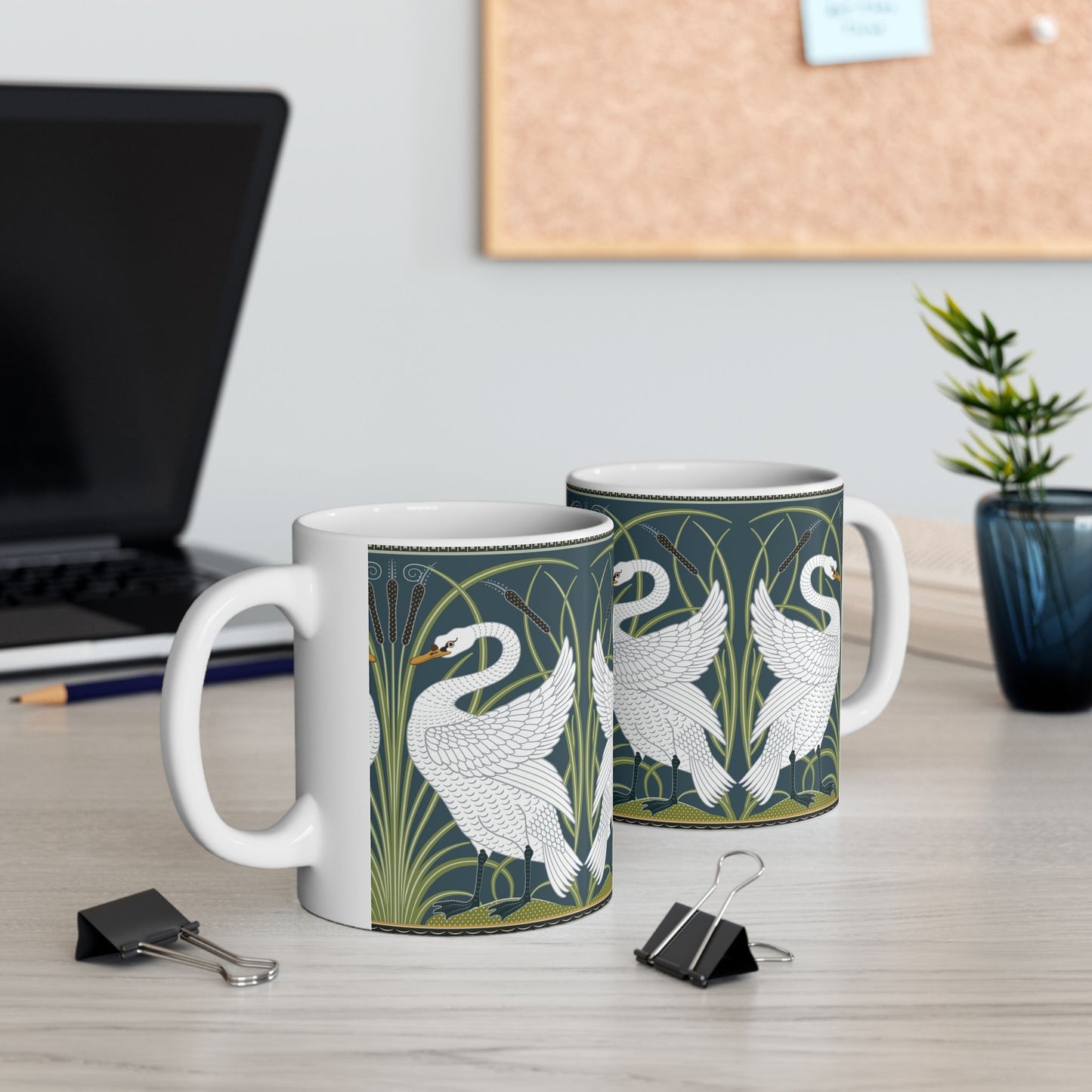 A ceramic mug with a design of two white swans on a green and blue background, inspired by the art of William Morris.