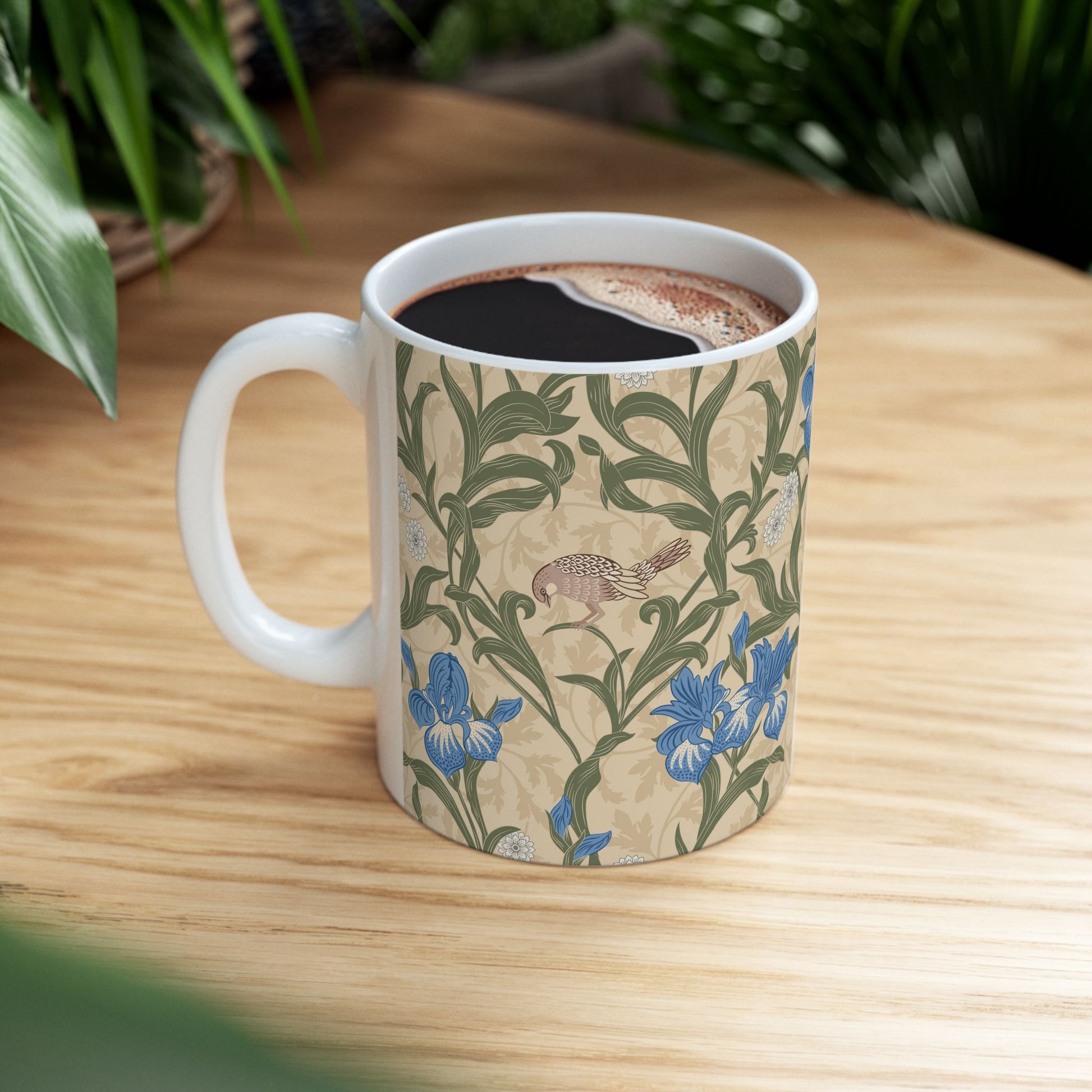 A ceramic mug with a floral William Morris & Co pattern design, featuring a bird and various flowers in shades of blue, green and beige.