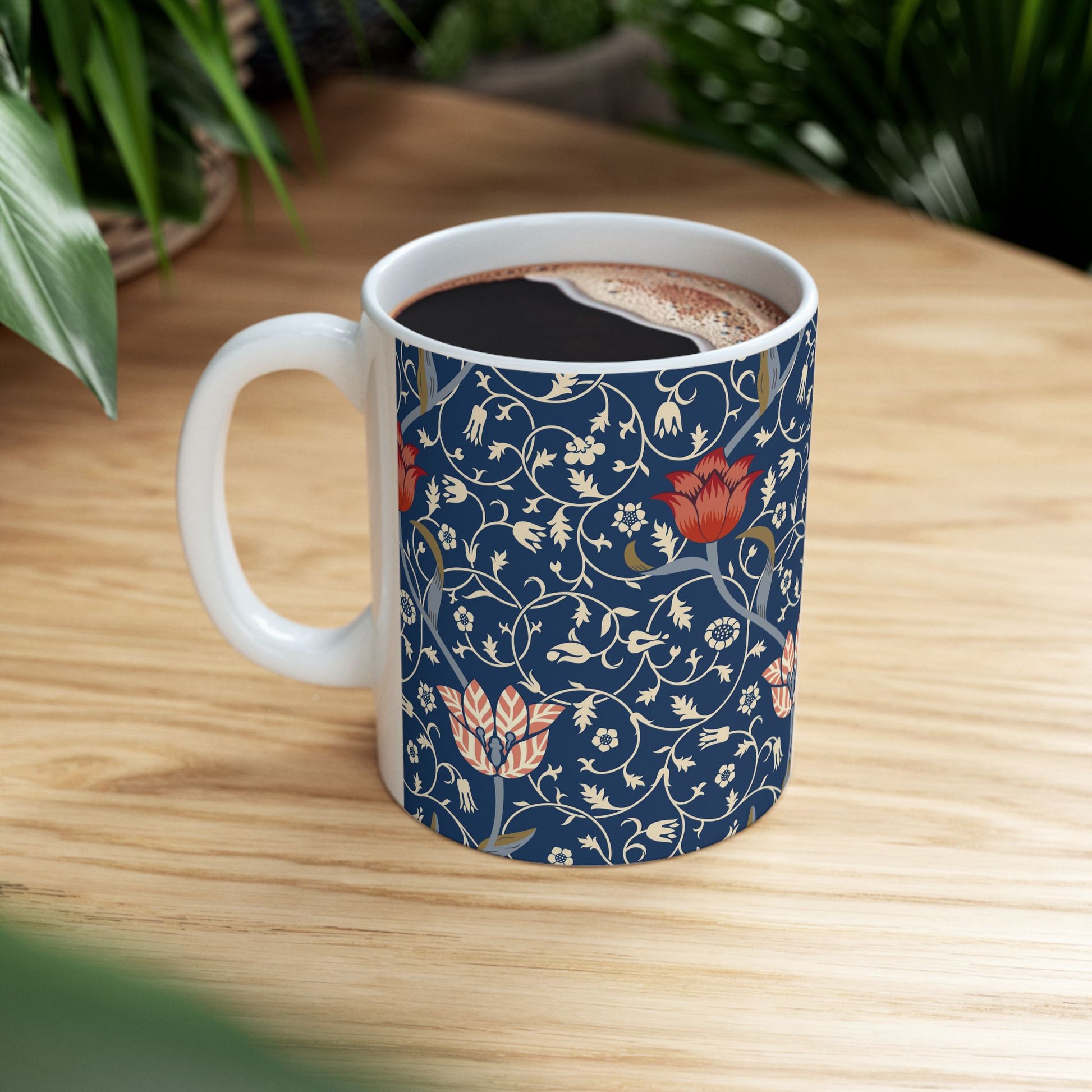 A ceramic mug with a floral pattern and a white handle featuring a blue. white, red and pink pattern design called Medway by William Morris & Co