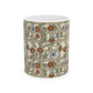 A white ceramic mug with a wrap-around Art Nouveau style print featuring a beige trellis pattern decorated with red flowers, green leaves, and blue butterflies.