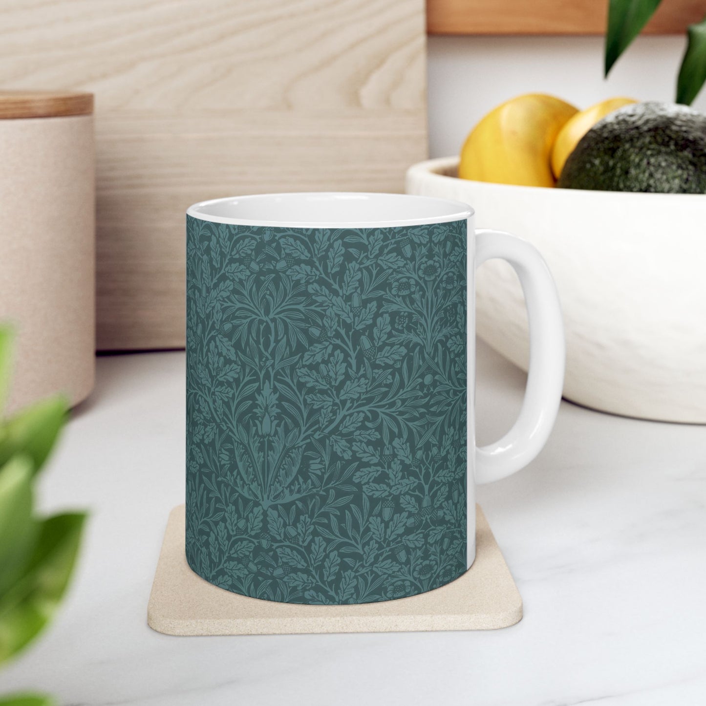 A ceramic mug with a teal base and a white handle featuring a floral and acorn pattern design, inspired by William Morris.