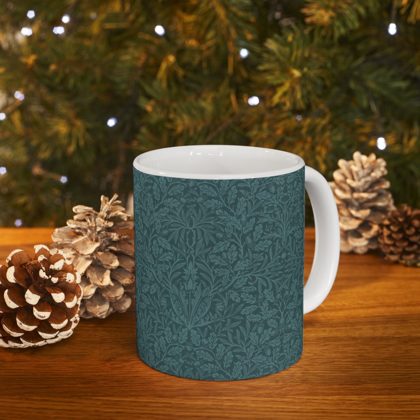 A ceramic mug with a teal base and a white handle featuring a floral and acorn pattern design, inspired by William Morris.