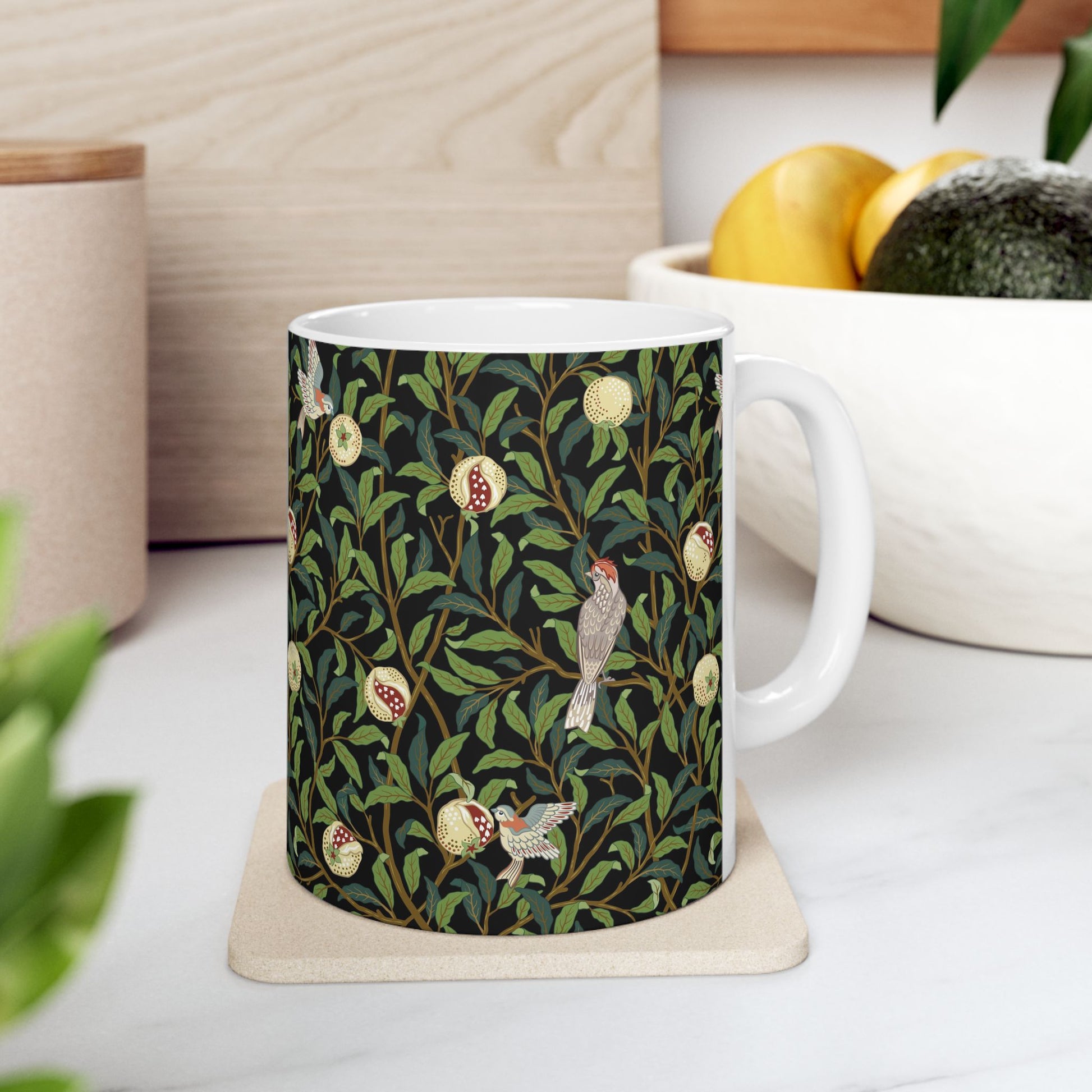 A ceramic mug with a black background featuring a floral William Morris & Co pattern of birds and pomegranates.