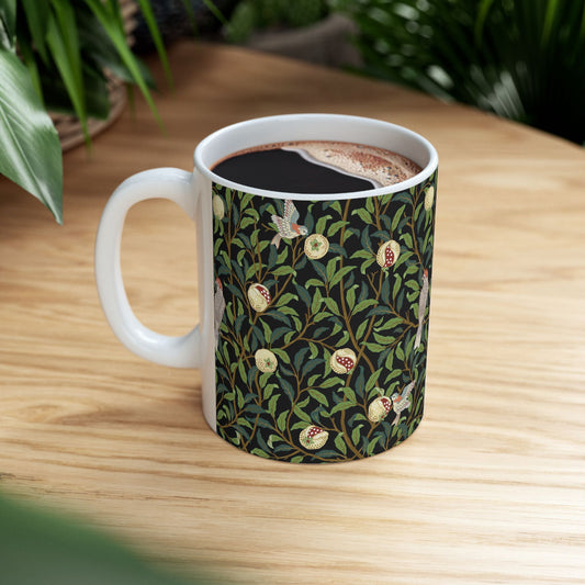 A ceramic mug with a black background featuring a floral William Morris & Co pattern of birds and pomegranates.
