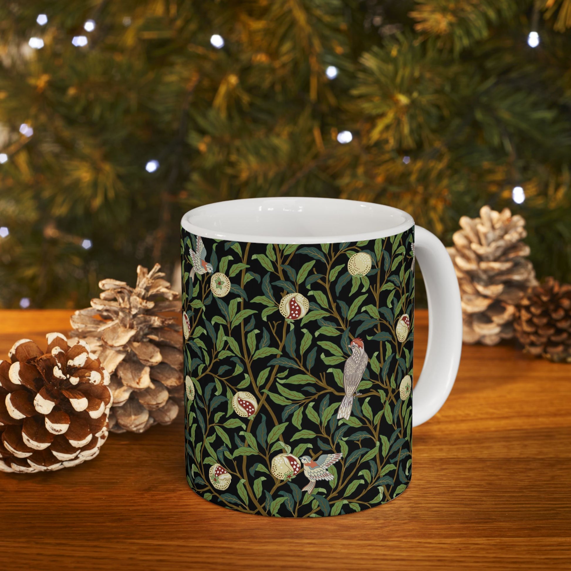 A ceramic mug with a black background featuring a floral William Morris & Co pattern of birds and pomegranates.