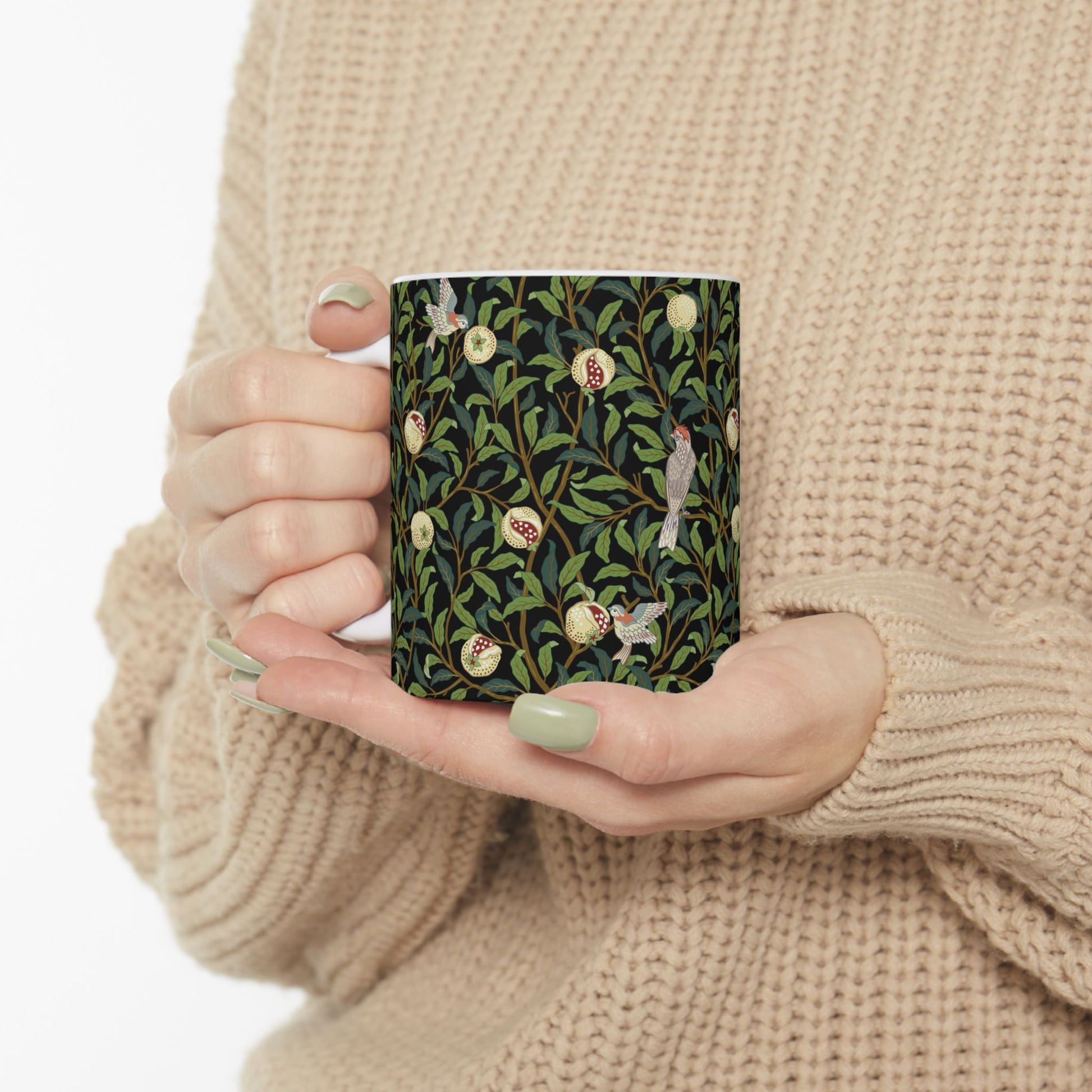 A ceramic mug with a black background featuring a floral William Morris & Co pattern of birds and pomegranates.
