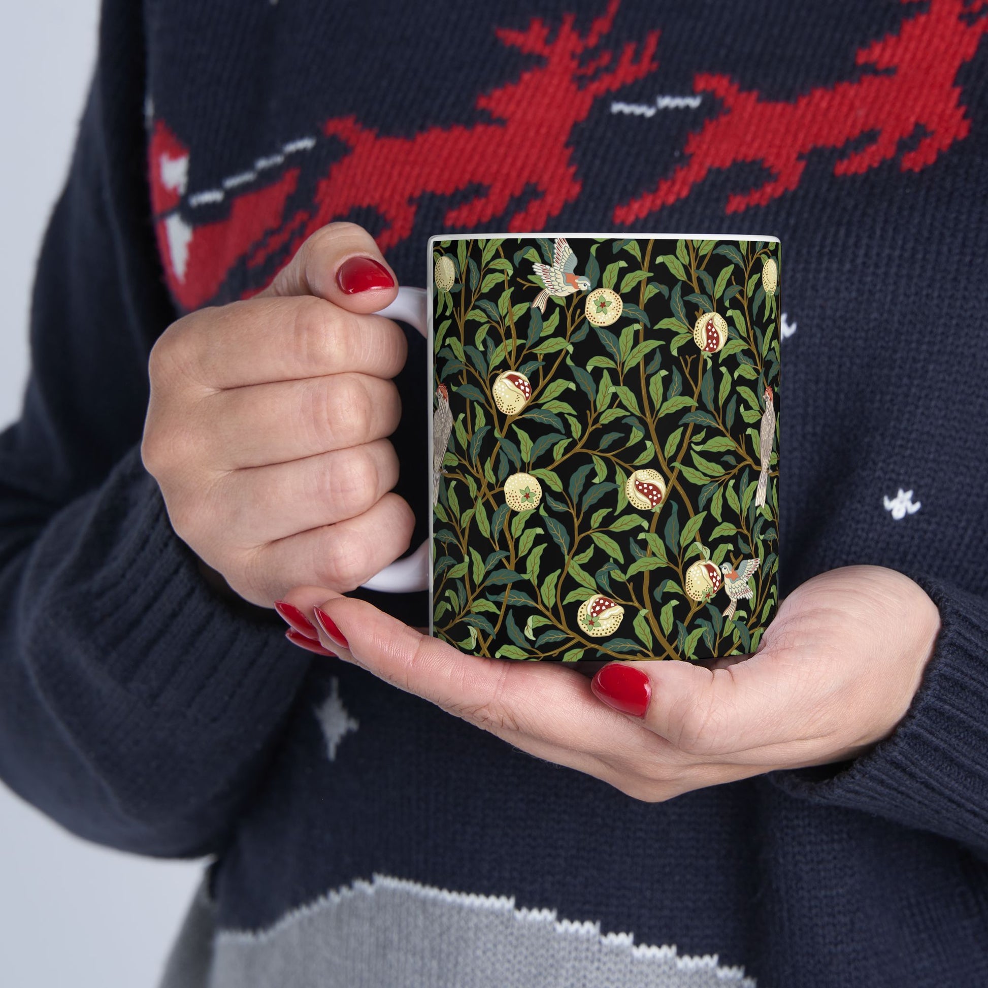 A ceramic mug with a black background featuring a floral William Morris & Co pattern of birds and pomegranates.