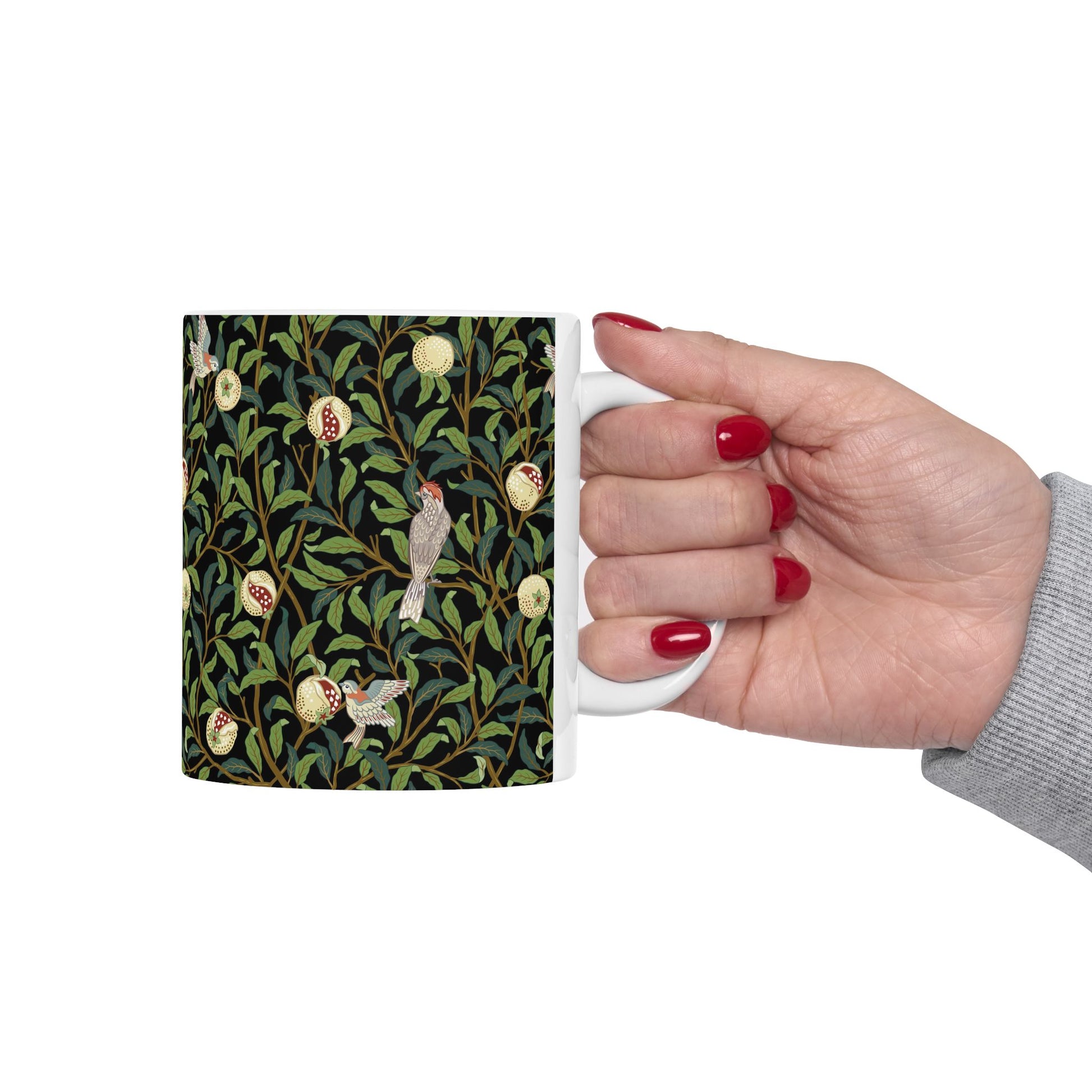A ceramic mug with a black background featuring a floral William Morris & Co pattern of birds and pomegranates.