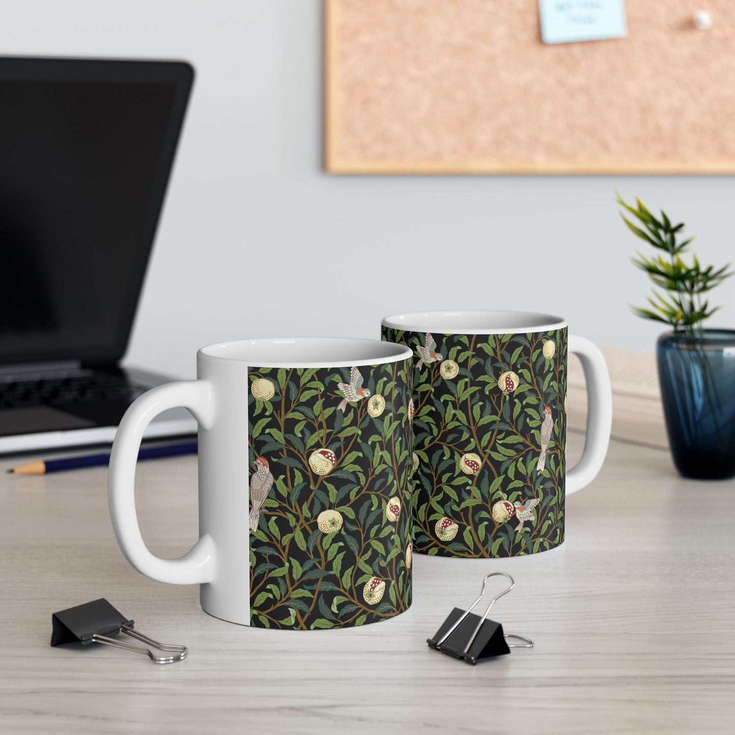 A ceramic mug with a black background featuring a floral William Morris & Co pattern of birds and pomegranates.