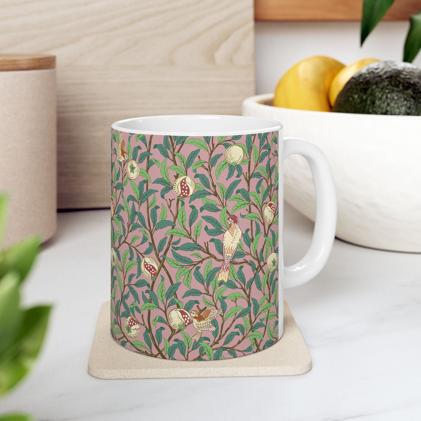 A white ceramic mug with a pink floral and pomegranate design inspired by William Morris.
