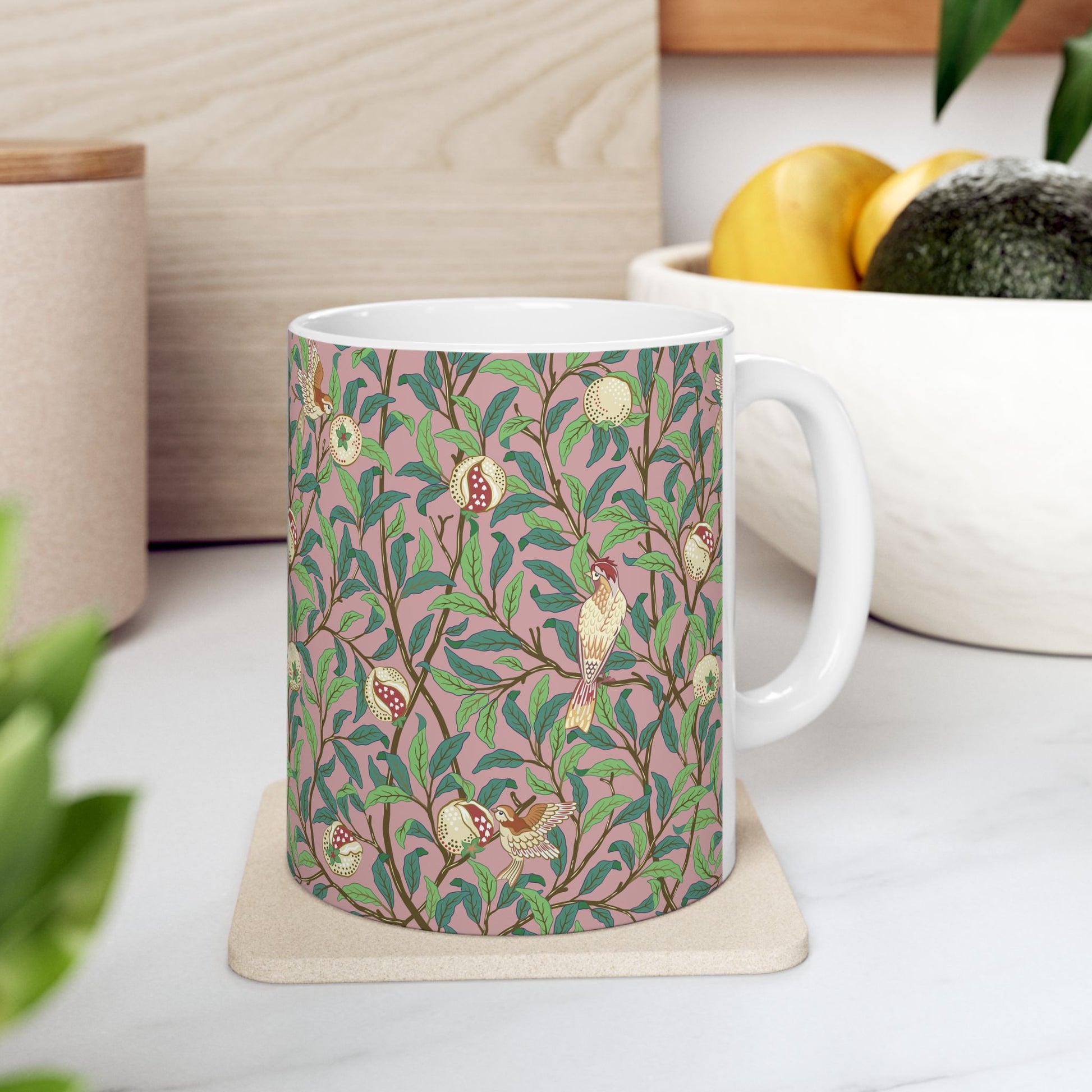 A white ceramic mug with a pink floral and pomegranate design inspired by William Morris.