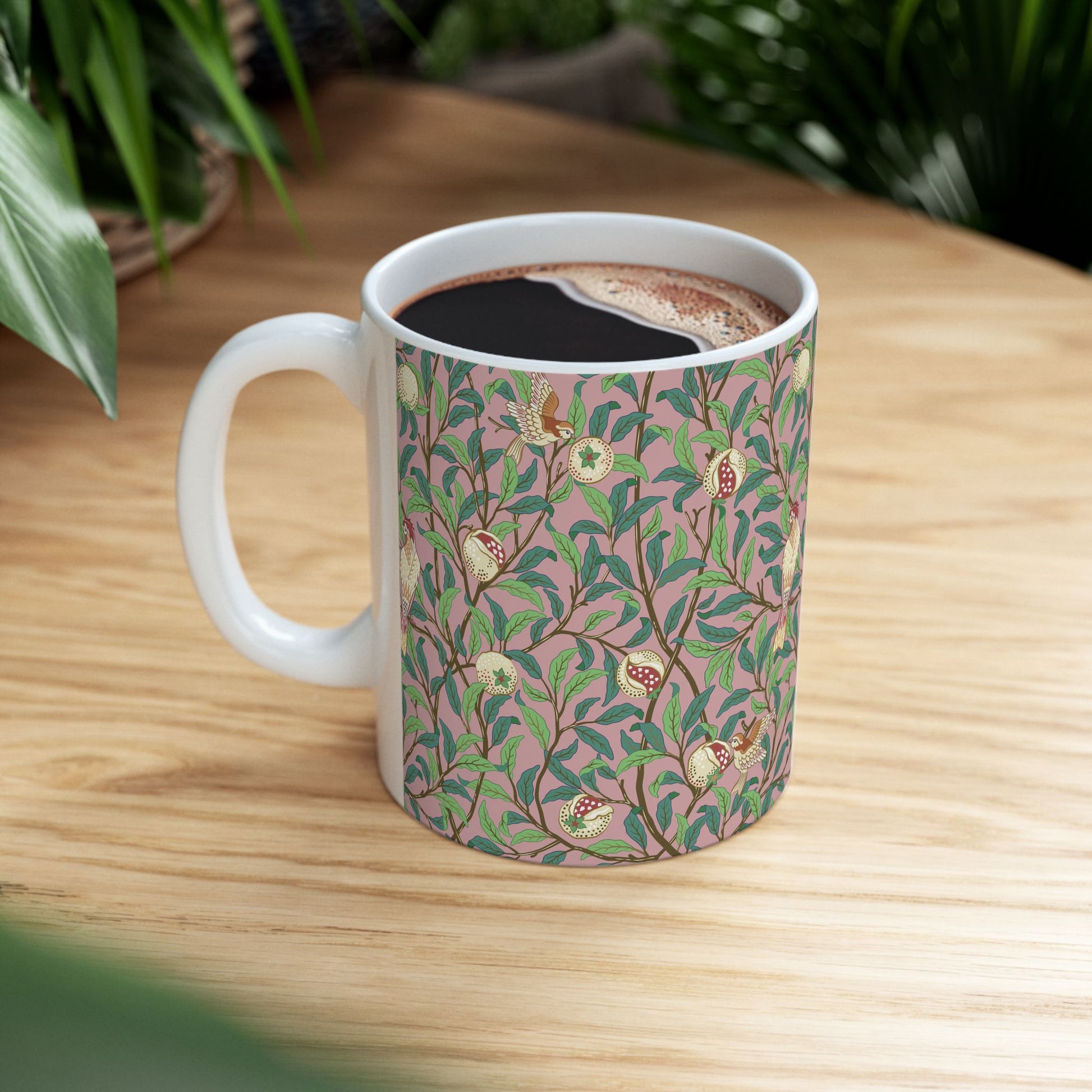 A white ceramic mug with a pink floral and pomegranate design inspired by William Morris.
