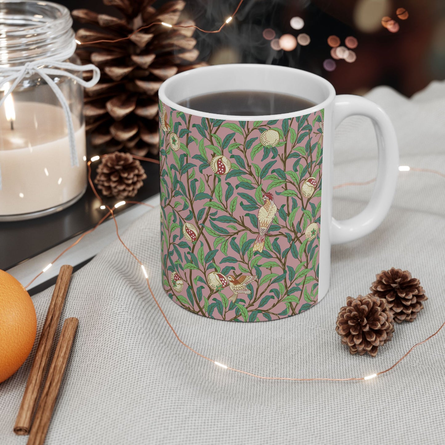 A white ceramic mug with a pink floral and pomegranate design inspired by William Morris.