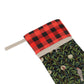 A Christmas stocking with a floral and bird design, featuring a black and white plaid pattern at the top and a wood loop for hanging.