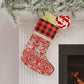 Red and white patterned Christmas stocking hanging by a fireplace with a plaid top section.