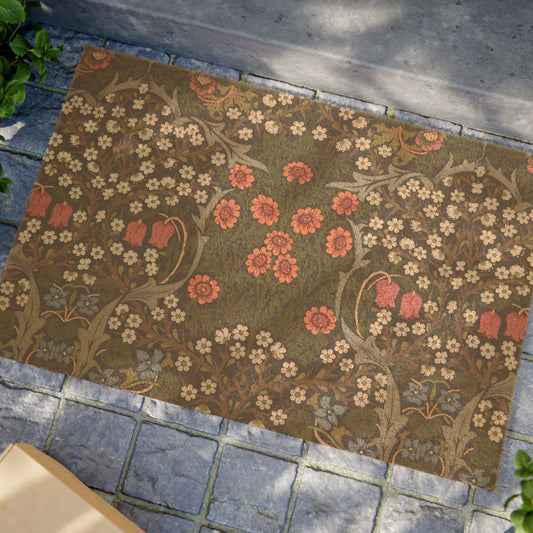 A rectangular area rug with an intricate floral and botanical pattern in muted olive green, terracotta, and cream, laid out on a gray stone patio.